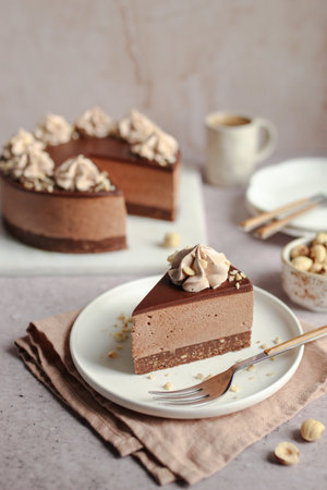 No-bake Nutella cheesecake with chocolate ganache and hazelnuts on a white plate. Cup of coffee in the background.の写真素材