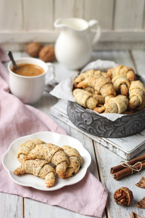 Walnut crescent cookies filled with plum jam on a white plate. Cup of coffee, a white milk jug, and a pink napkin. White wooden table and white rustic wooden background.の写真素材