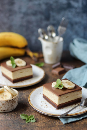 Two pieces of chocolate banana cake on a plate, decorated with banana slices and fresh mint leaves. Dark brown base and blue background.の写真素材
