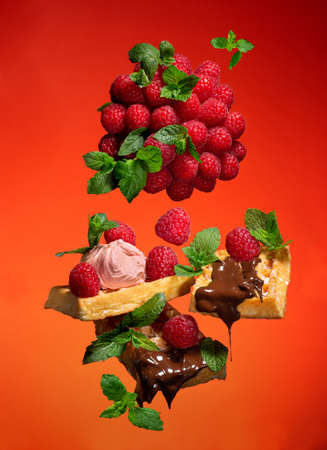 Levitation with Viennese waffles, raspberries, mint leaves with chocolate icing on a red-orange backgroundの写真素材