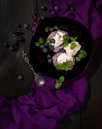 blueberry soft ice cream with blueberries, on a black dish, on a black wooden table and a purple napkinの写真素材