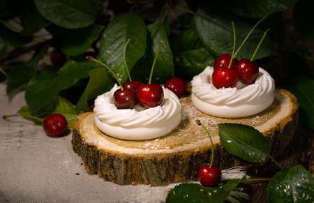 white meringue, meringue with cherry berry on a wooden cut on a brown wooden table and cherry leavesの写真素材