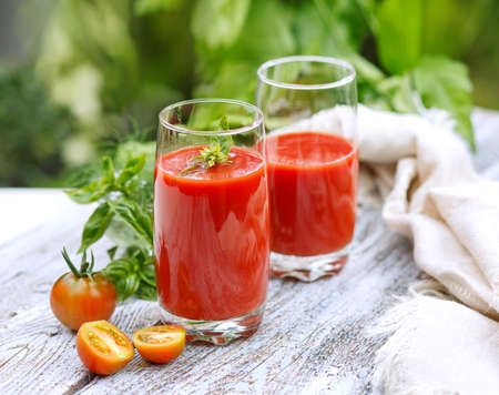 Fresh tomato juice in glass glasses, with tomato slices on a light wooden table in the garden against the backdrop of greeneryの写真素材