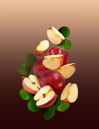 ripe whole red apples with cut slices, with green leaves on a gradient beige-brown background hanging in the air.の写真素材