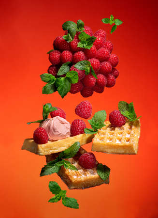 Levitation with viennese waffles, raspberries, mint leaves on a red-orange backgroundの写真素材