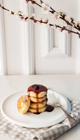 Breakfast in the morning. Cottage cheese pancakes with jam on white plate. Russian, Ukrainian cuisine. Spring flowersの写真素材