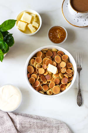 Mini pancake cereal with butter on white background. Cup coffe, sour cream and jam. Trendy Food...