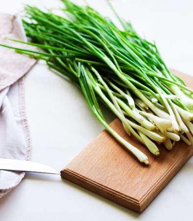 Slicing fresh green spring onions on a wooden board on a white backgroundの写真素材