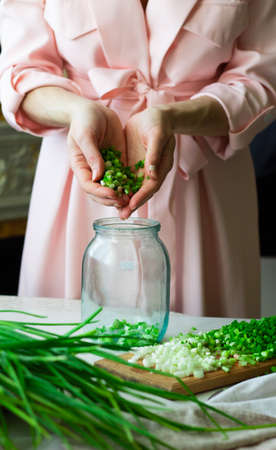 Pickled onions in a jar. Female hands poured into a jar finely chopped green onions. Fermented foodの写真素材