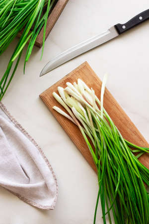 Slicing fresh green spring onions on a wooden board on a white backgroundの写真素材