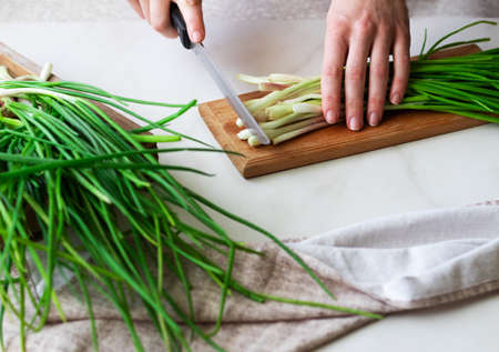 Female hands with a knife, slicing fresh green spring onions on a wooden board on a white backgroundの写真素材