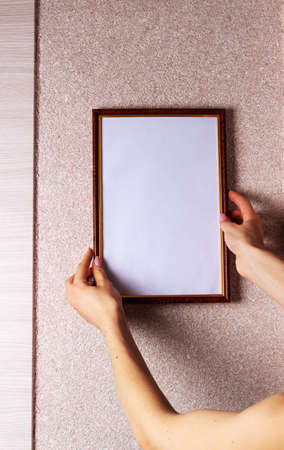Woman hangs poster mockup with rectangular frame hanging on the wallの写真素材