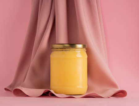 Ghee or clarified butter in jar with pink silk fabric on pink background. Minimal style. Copy space.の写真素材