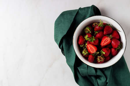 Fresh strawberries in plate with green napkin on marble white table. Minimal concept with copy space for text.の写真素材