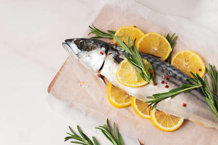 Fresh fish with lemon, rosemary, salt and pink pepper on wooden board and parchment.の写真素材