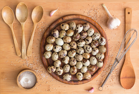 wooden spoons, salt, quail eggs, seeds crushed wheat, garlic, whisk, cutting Board on wooden background. Still life with quail eggs.の写真素材