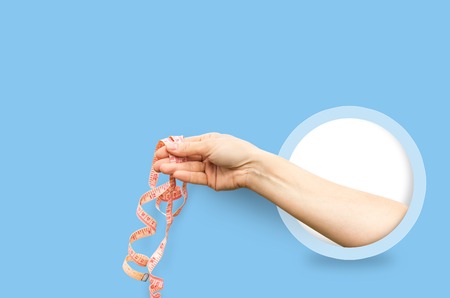 Beautiful woman hand stretching a measure tape isolated on a blue background