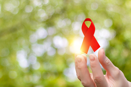 Ribbon for the fight against AIDS in the hands on blurred background.