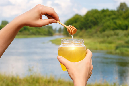 Flowing honey in glass pot on a background of the river.の写真素材