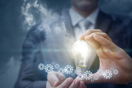 Light bulb with gears in the hands of the businessman. The concept of the idea while working.の写真素材
