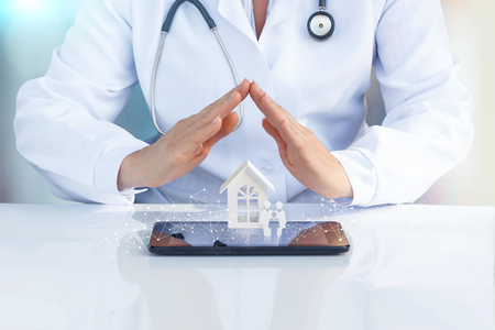 Doctor at the table with his hands to protect the icon the family and home. The concept of health insurance of the family.