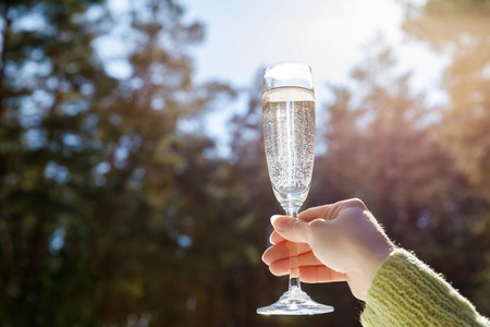 Glass of champagne in hand on the background of trees and sky.の写真素材