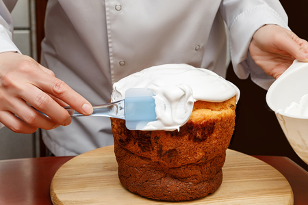 Cook misses with a spatula cream cake on a dark background.