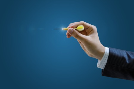 Hand of a businessman to aim with a dart on a blue background.の写真素材