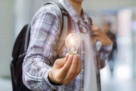 Student shows a burning light bulb. The concept of doctrine as the light.の写真素材