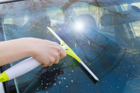 Scraper in hand cleans the glass of the car.