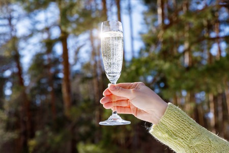 A glass of champagne in hand on background of a winter forest.の写真素材