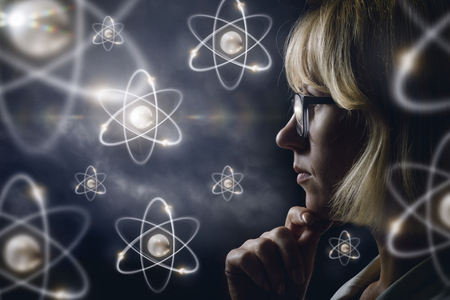 Woman looking explores atoms on a dark background.