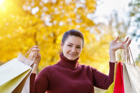 A smiling women holding the purchases in her arms at the background with yellow leaves.の写真素材