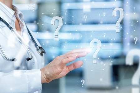 A doctor dressed in the medical uniform showing the interrogation marks standing inside the innovative medical room. The concept is the professional support in finding the correct solution.の写真素材