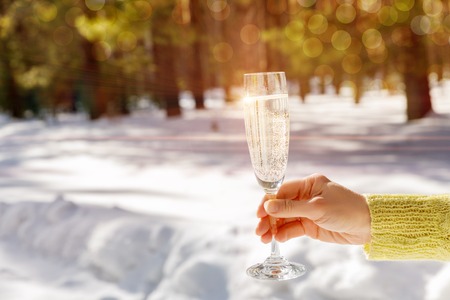 A hand holding a glass of fizzing champagne against the snowy winter background. The concept is the happy New Year holiday celebration.の写真素材