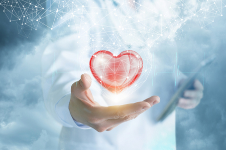 A doctor is showing a bright heart in the digital connections cage with a cloud of wireless connections above at the blurred background.の写真素材