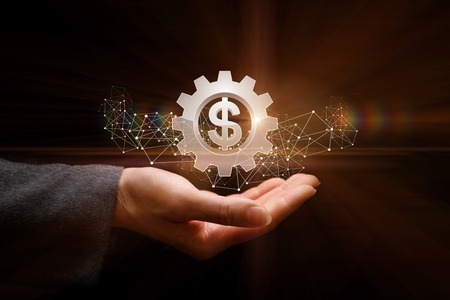 A businessman is holding a cogwheel in his hand with currency unit inside. The concept is the ability of money operation.の写真素材
