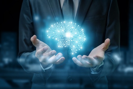 A brain image consisted of different connections with the chip inside is hanging between the businessman's hands at the dark background. The concept is the artificial intelligence and brainstorming.の写真素材