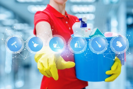 A cleaning woman in rubber gloves is keeping a bucket fulfilled with chemicals and touching a screen with digital scheme of many symbols. The concept is the popularity of cleaning service.の写真素材