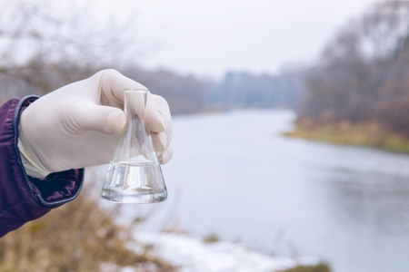 A laboratorian is holding a test tube with transparent river water sample inside at the river bank background.の写真素材
