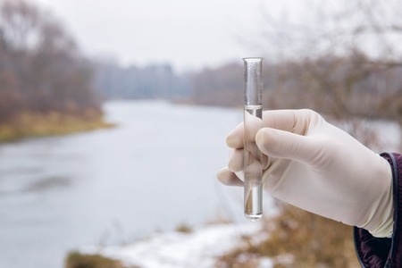 A laboratorian test tube with river water sample in the hand of a specialist at the autumn nature background. The concept is the environment ecology.の写真素材