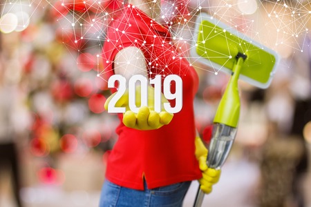 A cleaning woman in rubber gloves with a mop in one hand is showing the numbers of coming year in...