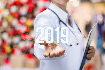 A doctor with a stethoscope is showing the numbers of coming year in her hand at the bright lights background. The concept is the future development of medical service.の写真素材