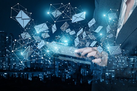 A businesswoman is working with a device against the busy city and networking system onsisted of wireless connections and envelope icons background. The concept is the usage of social networks in everyday and business life.の写真素材