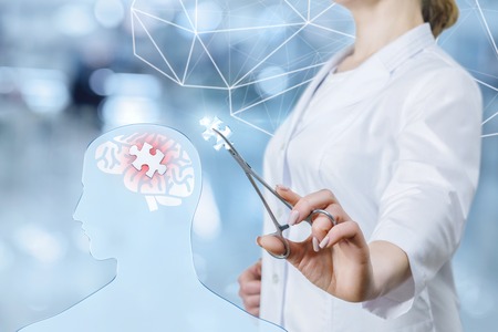 A young doctor is standing sideways and putting the missing puzzle into the irritated brain model of...