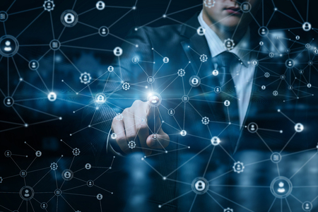 A businessman is performing with social networking structure of wireless connections with human figures icons and cogwheels at blurred city background. The concept is social networking principle.の写真素材