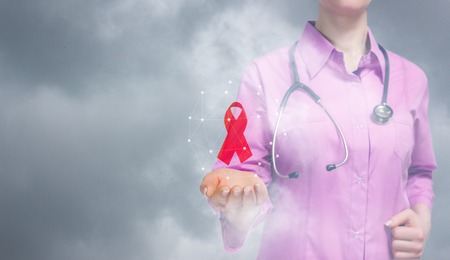A closeup of doctor with red aid ribbon as awareness, charity and support symbol in dangerous diseases hanging above her hand inside the wireless connections sphere. The world aids day concept.の写真素材