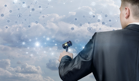 A closeup of a man standing backside with a hammer in his hand in front of digital social network system of wireless connections and human figures icons. The concept of public and online auction.の写真素材