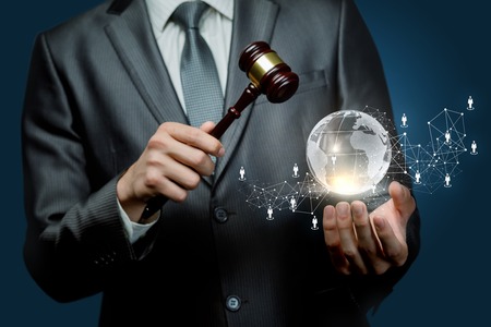 A closeup of a man holding a hammer and a globe with social network system with human figures icons at dark background. The concept of international auction.の写真素材