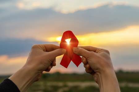 Aids red ribbon in hands on the background of sunset.の写真素材